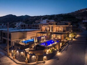 A modern multi-story residential building with a swimming pool and outdoor lighting. - Lapis Nera Villas (Viannos)