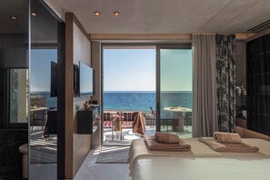 A modern hotel room with a large bed, a TV, and a view of the sea. - Lapis Nera Villas  (Viannos)