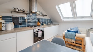 Una cucina moderna con piano cottura a gas, forno e cappa aspirante in acciaio inox. C'è una zona pranzo con tavolo e sedie, e una finestra che lascia entrare luce naturale.