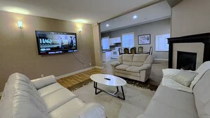 A modern living room with white leather sofas, a coffee table, and a flat-screen TV mounted on the wall. - Modern 2BR Walk-Out Suite | 2 Baths | Free Parking (Kelowna)