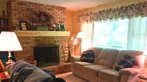 A cozy living room with a brick fireplace, a sofa, a chair, and a lamp. - NEW LISTING 15% OFF 5BR Lake Michigan Cottage Private Retreat • Family Friendly (Pentwater)