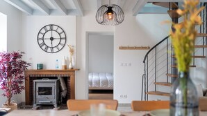 Un salon moderne avec une cheminée, une table à manger dressée pour deux personnes, un escalier et une grande horloge murale.