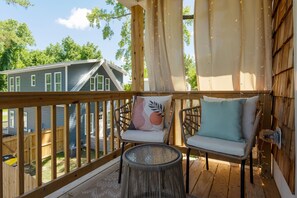 Eine Holzterrasse mit zwei Korbstühlen, einem kleinen runden Tisch und Blick auf ein Haus im Hintergrund.