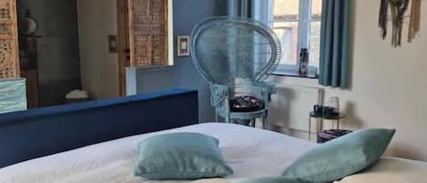 Un dormitorio con una cama grande, una silla, un ventanal con cortinas y una pared decorada con un atrapasueños.