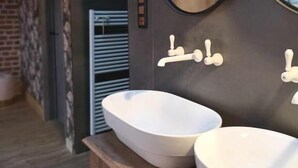 Un baño con dos lavamanos blancos tipo pedestal, un mueble de tocador de madera y dos espejos fijados a la pared.