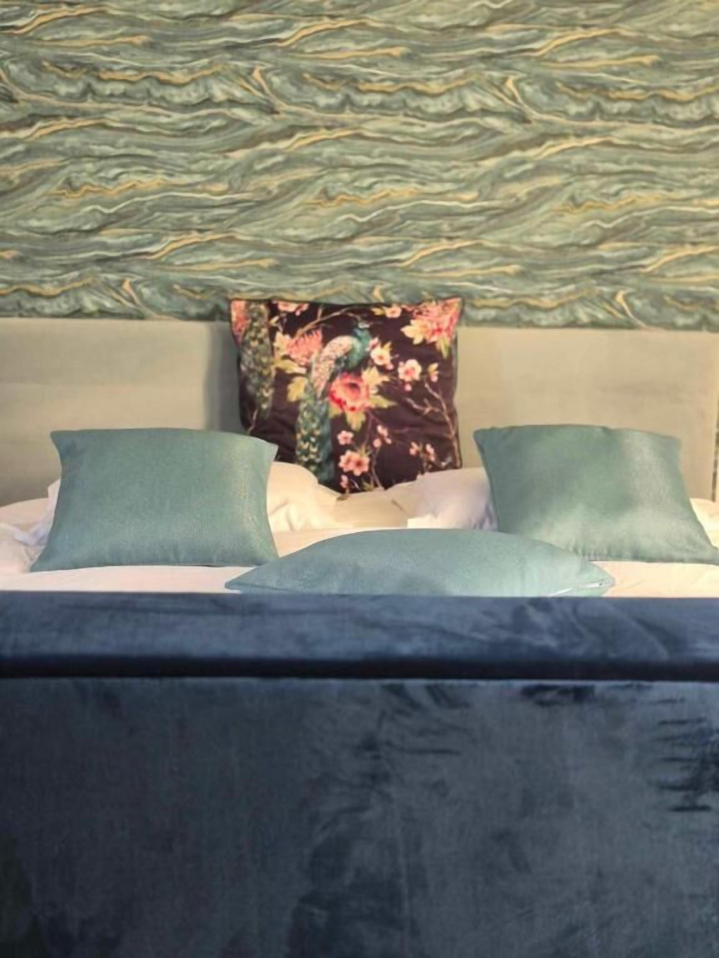 A bed with a floral pillow, a green pillow, and a blue blanket.
