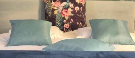 Una cama con un cojín floral, un cojín verde y una manta azul.