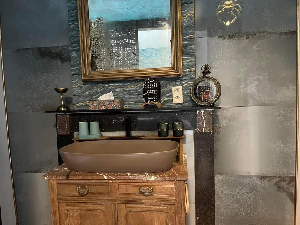 Un baño con un lavamanos ovalado grande, tocador de madera y un espejo con marco decorativo.