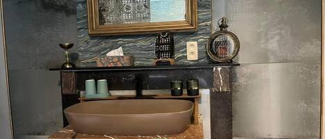 Un baño con un lavamanos ovalado grande, tocador de madera y un espejo con marco decorativo.