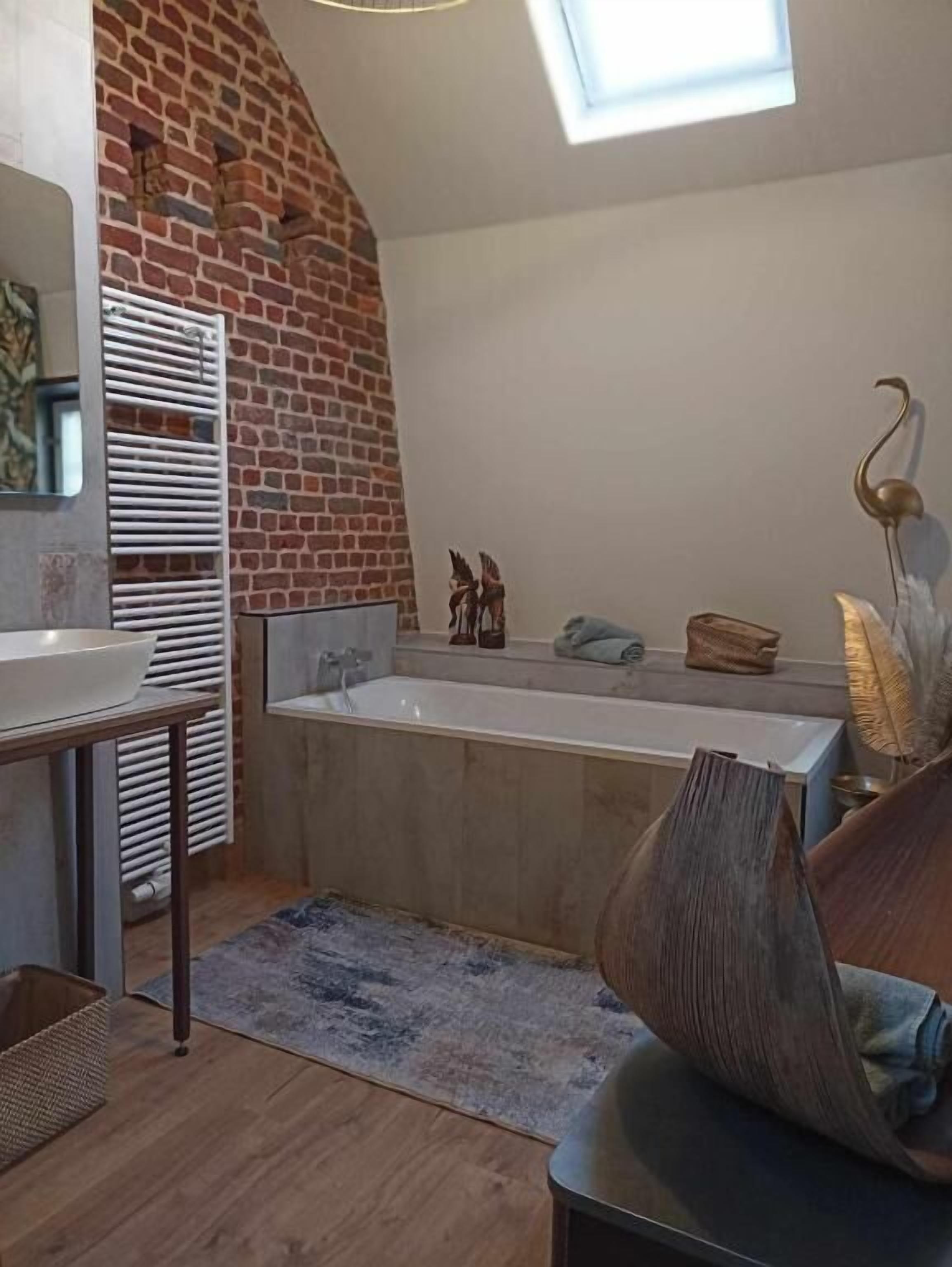 Un baño moderno con pared de ladrillo, una bañera independiente y un tragaluz.