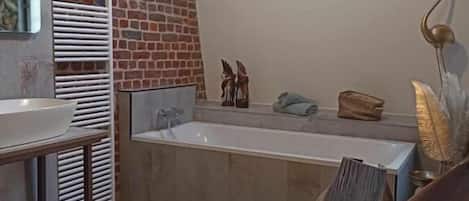 A modern bathroom with a brick wall, a freestanding bathtub, and a skylight.