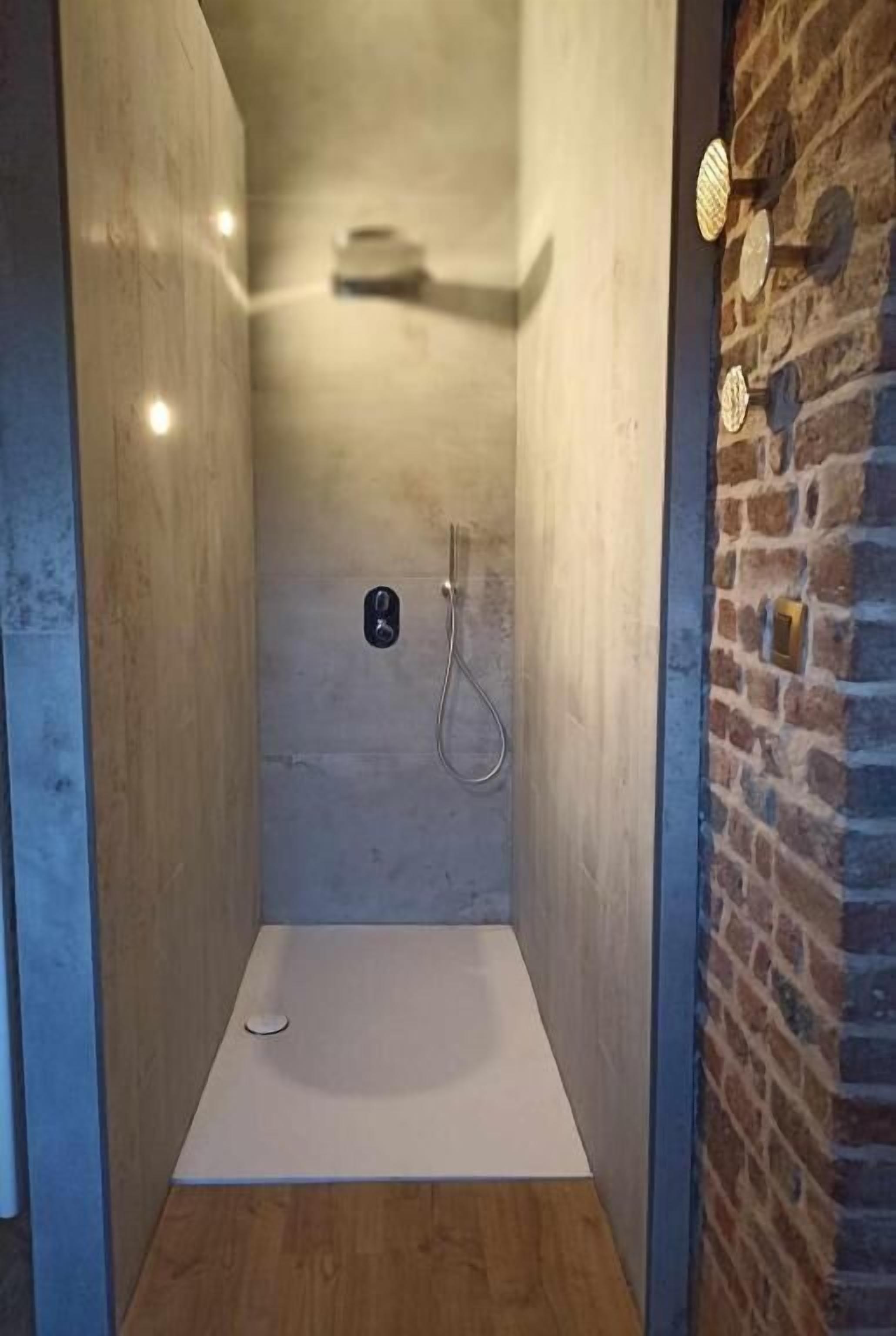 A shower area with a tiled floor, a showerhead, and a wall-mounted control panel.