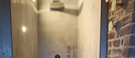 A shower area with a tiled floor, a showerhead, and a wall-mounted control panel.
