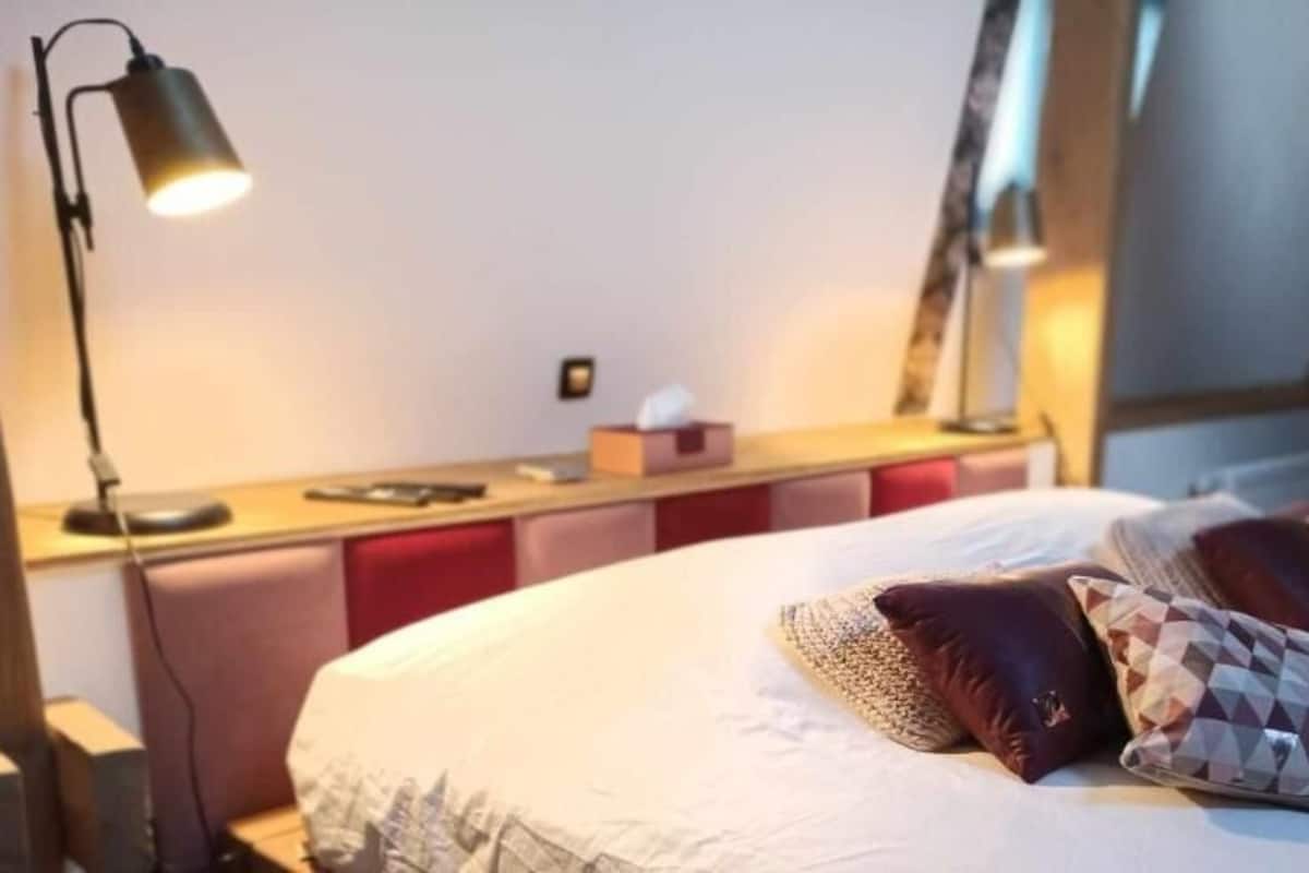 A neatly made bed with patterned pillows, a bedside lamp, and a small table with a tissue box.