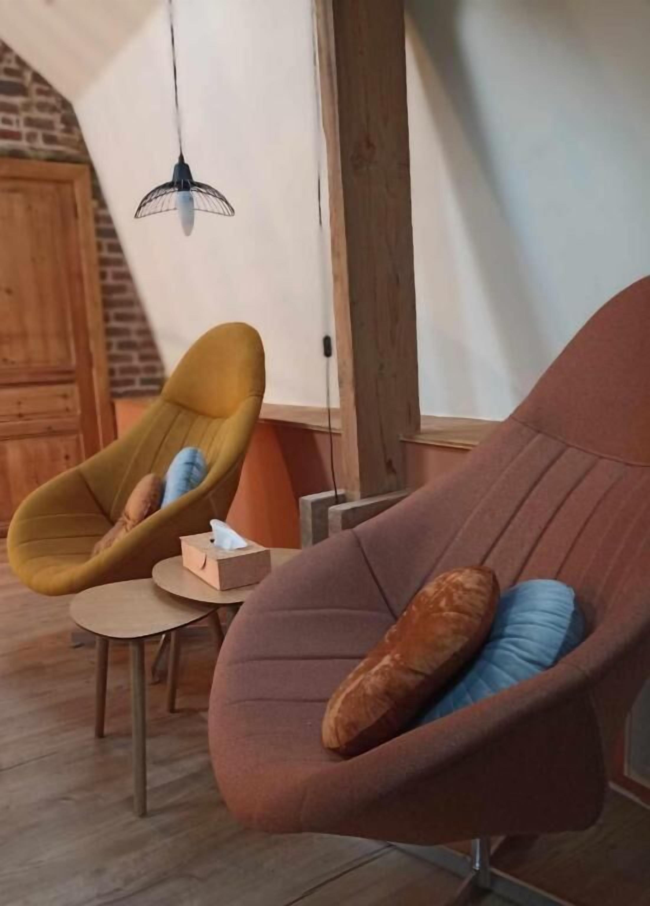 Un salon moderne avec un plafond en bois, un luminaire suspendu et deux fauteuils avec des coussins.