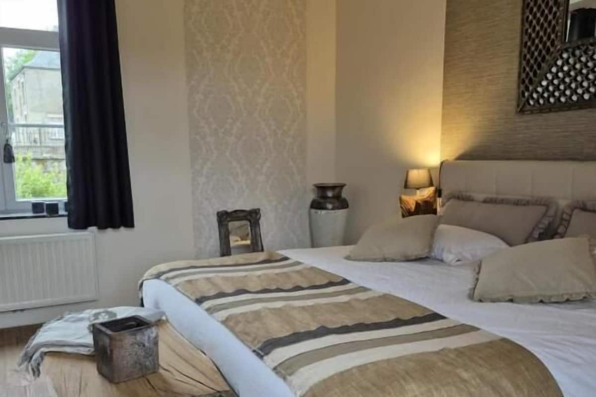 A bedroom with a large bed, a bedside table, a lamp, and a window with curtains.