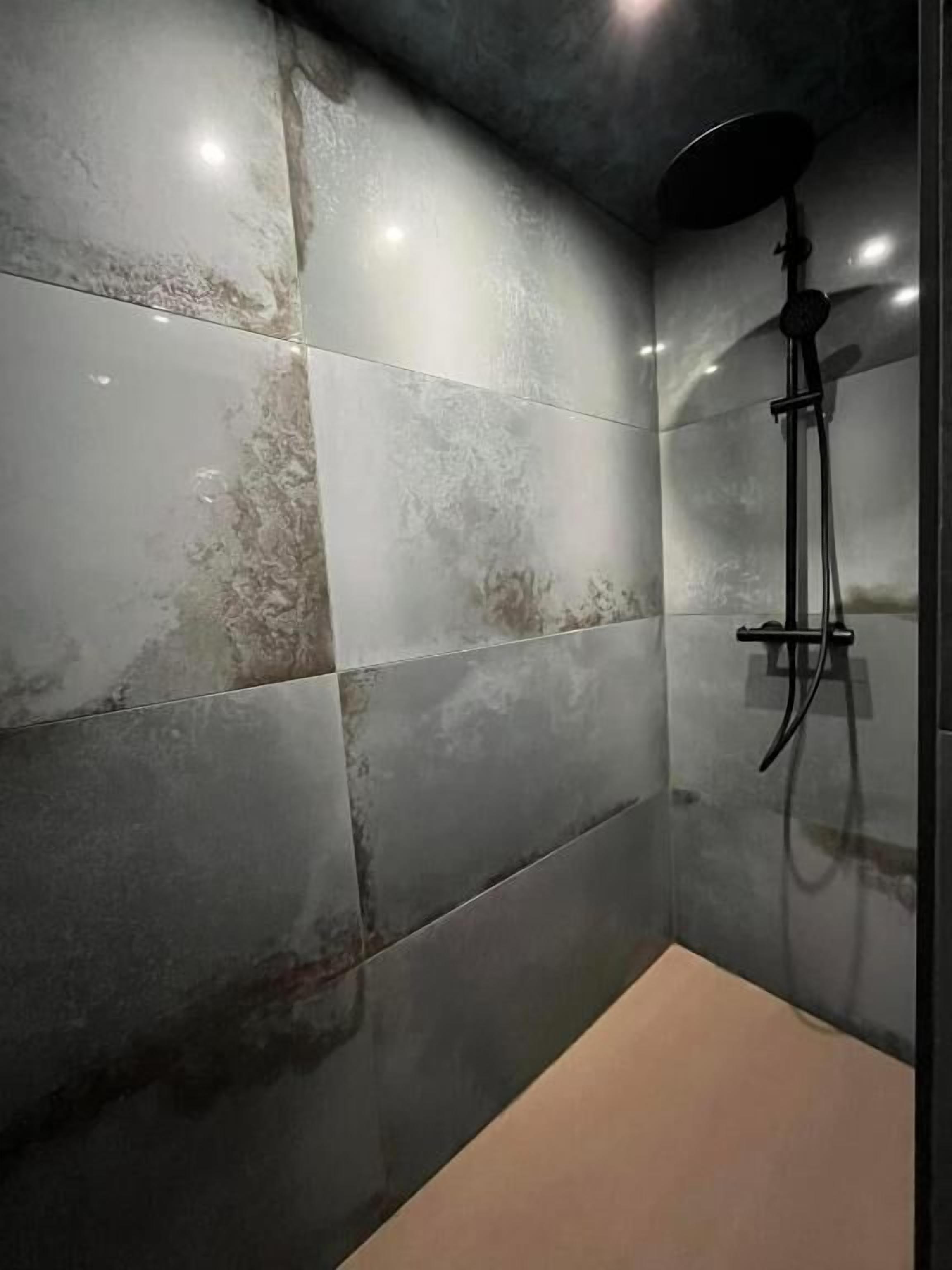 A modern shower area with grey tiles and a handheld showerhead.
