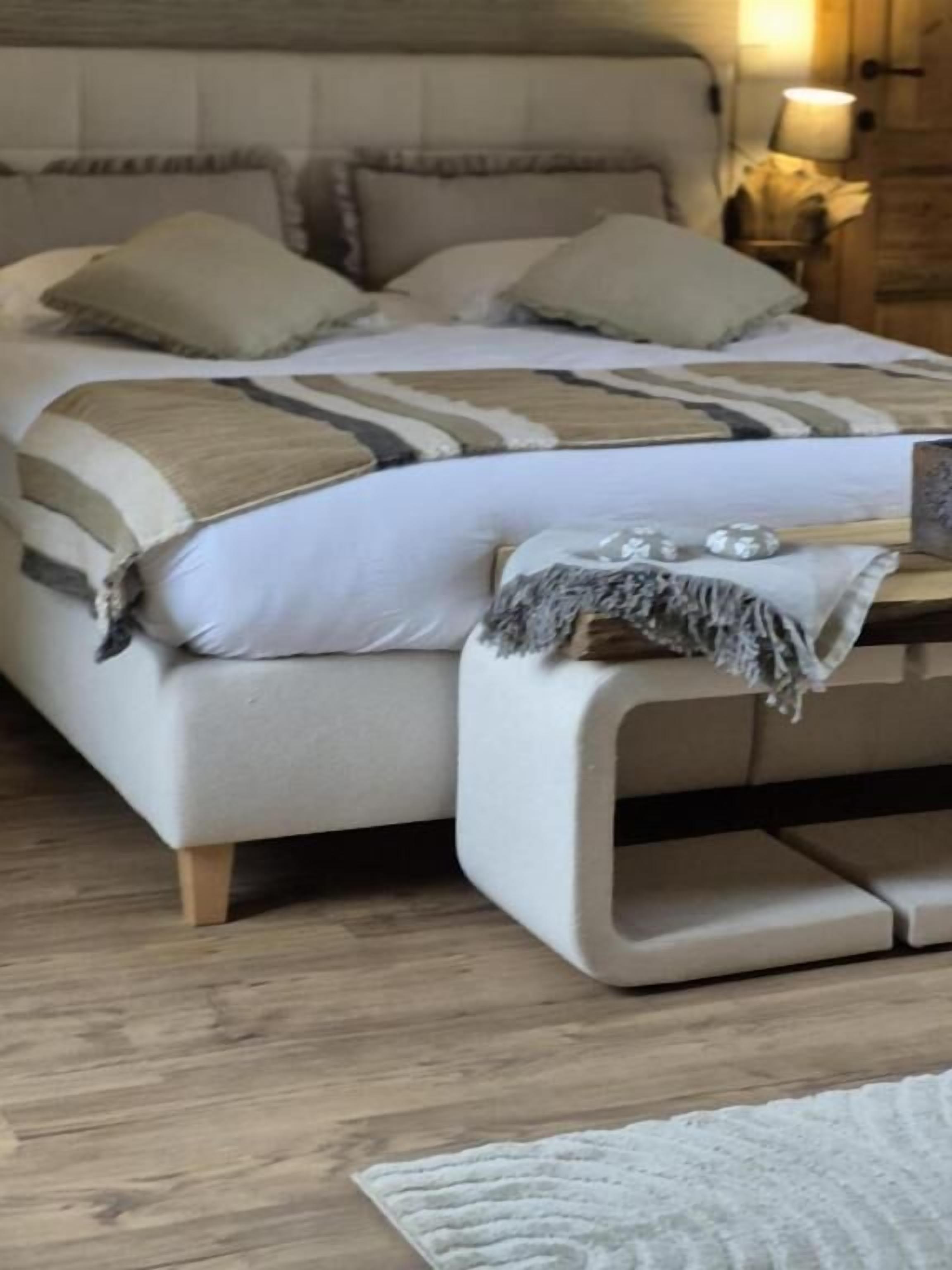 Ein Bett mit beigefarbenem Kopfteil, mehreren Kissen und einer Decke.
