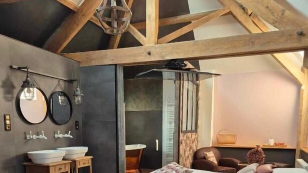 Un dormitorio con una cama grande, vigas de madera, un tocador con lavamanos y una silla.