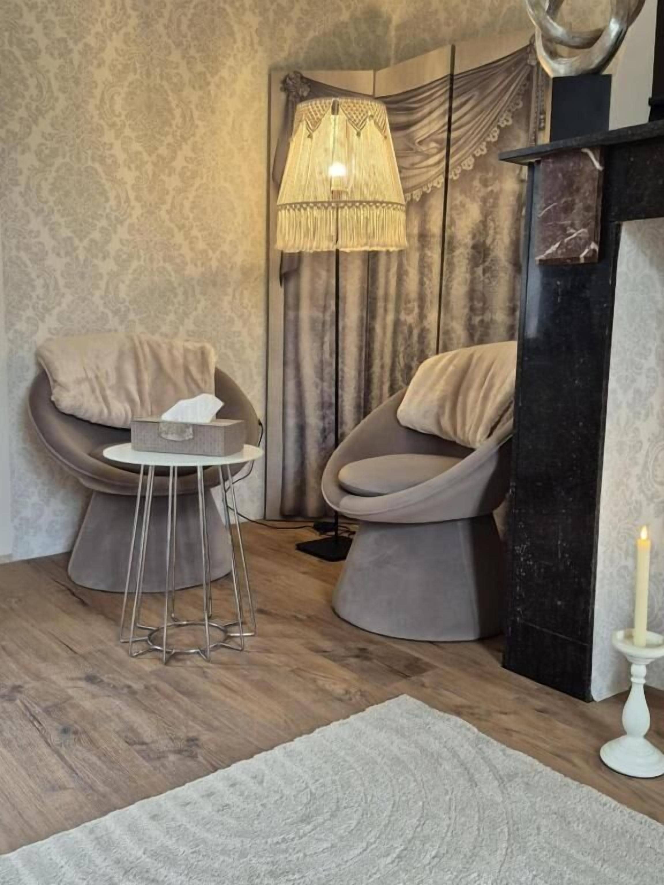 A modern living room with two armchairs, a small round table, a decorative lamp, and a fireplace.