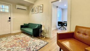Ein Wohnzimmer mit einem grünen Sofa, einem braunen Ledersessel, einem gemusterten Teppich und einem Essbereich mit Tisch und Stühlen.