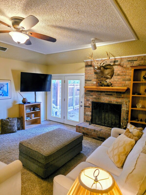 A living room with a fireplace, a ceiling fan, a television, and a bookshelf.