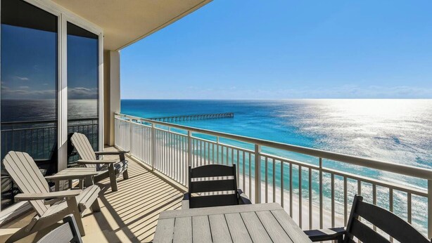 Un balcone con vista sull'oceano e un molo. Sul ponte ci sono sedie e un tavolo in legno.