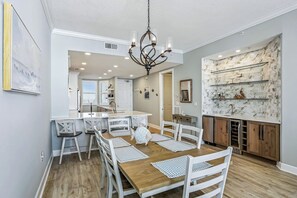 A modern kitchen with marble backsplash, wooden cabinets, and a dining area with white chairs and a wooden table. - Pelican`s Flight: 2bed 2bath newly renovated condo 17th floor directly on the Gulf! Sleeps 6! (Gulf Breeze)