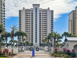 A high-rise hotel with a central tower, surrounded by palm trees and a gated entrance. - Pelican`s Flight: 2bed 2bath newly renovated condo 17th floor directly on the Gulf! Sleeps 6! (Gulf Breeze)