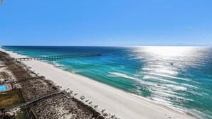 Una spiaggia con un molo che si estende nell'oceano, un litorale sabbioso e un cielo azzurro limpido.