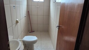 Une petite salle de bain carrelée, équipée de toilettes, d’un lavabo et d’une fenêtre.