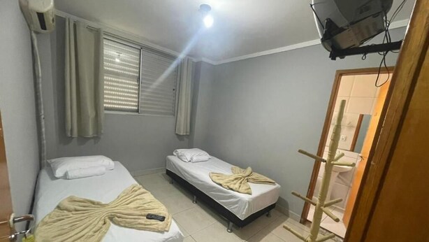 Une chambre d’hôtel avec deux lits, un ventilateur de plafond, une fenêtre avec des stores et une porte dotée d’un porte-manteau.
