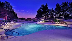 Ein Swimmingpool mit Liegestühlen und Sonnenschirmen, umgeben von Bäumen und blauem Himmel.