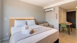 A hotel room with a large bed, a desk with chairs, a small sofa, and an air conditioning unit on the wall. - Modern Studio in Lapa With Pool and gym R1205 (Nova Iguaçu)