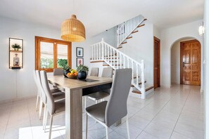 Ein Essbereich mit einem Holztisch, grauen Stühlen, einer hängenden Leuchte und einer Treppe mit Holzhandläufen.