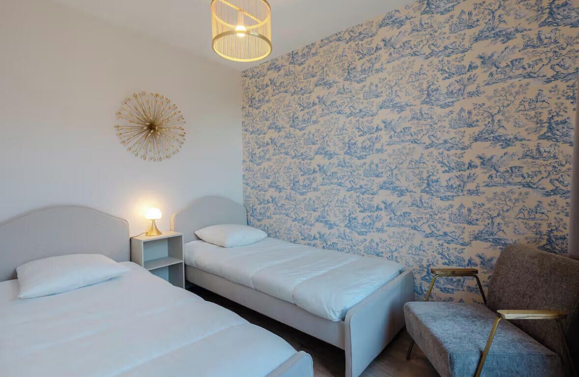 Un dormitorio con dos camas, una mesita de noche, una silla y una pared con estampado floral.
