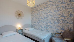 Quarto com duas camas, uma mesa de cabeceira, uma cadeira e parede com padrão floral.