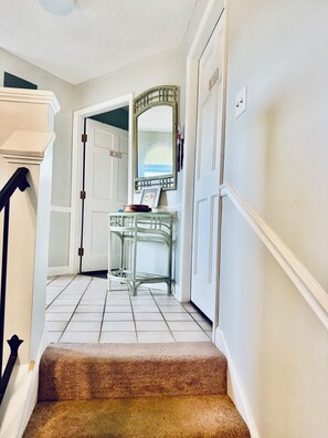 A staircase with a carpeted landing leading to a room with a white door, a mirror, and a small table with a bowl and picture frame. - Charming oceanfront 2BR condo with gorgeous views in North Topsail Beach, NC (North Topsail Beach)