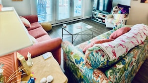 Un salon avec un canapé rouge, un divan aux couleurs vives, une table basse en verre et un téléviseur.