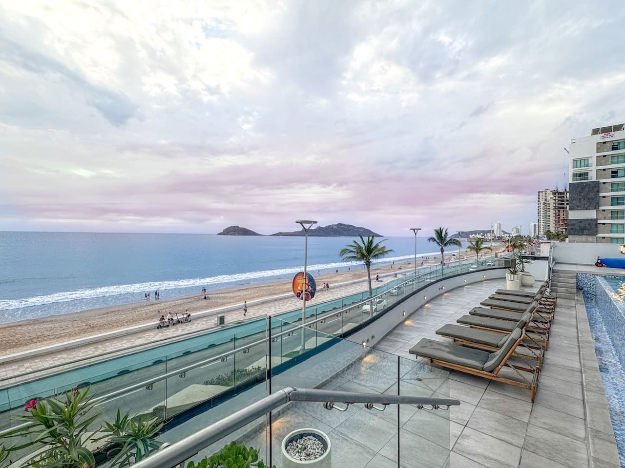 A rooftop terrace with a view of the beach and ocean, lounge chairs, and a swimming pool.