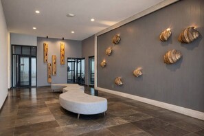 A modern lobby with a curved seating area, a reception desk, and decorative shell wall art. - Condo Premium - Malecón | Vista al mar | Grupos 6+ (Mazatlán)