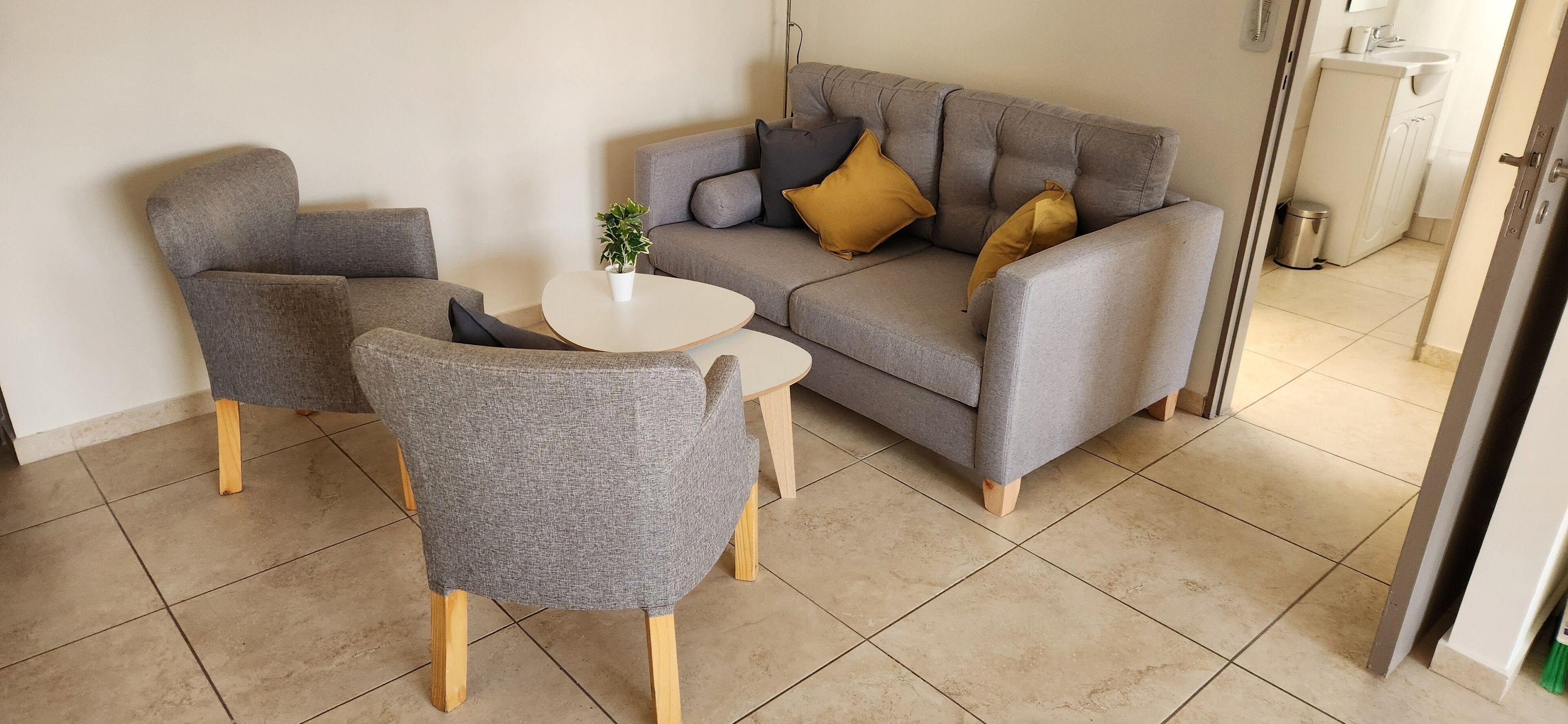A living room with a grey sofa, two armchairs, a small white table, and a potted plant.