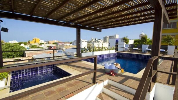 Area piscina sul tetto con vista sulla città, zona relax coperta e una scala che scende.