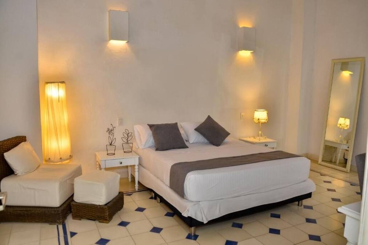 Ein Schlafzimmer mit einem großen Bett, Nachttischen, einem Sessel und einem Spiegel.