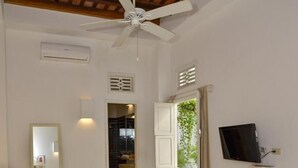 Una camera d'albergo con un letto, una scrivania, una sedia, una TV, uno specchio e una finestra con tende.