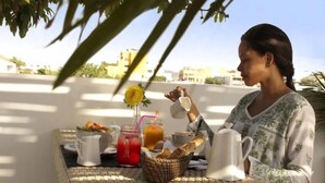 Una tavola apparecchiata per la colazione, con un boccale, un bicchiere di succo e un cestino di pane.