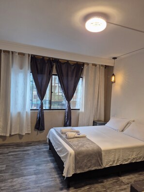 Un dormitorio con cama, cortinas, una ventana y una lámpara colgante.