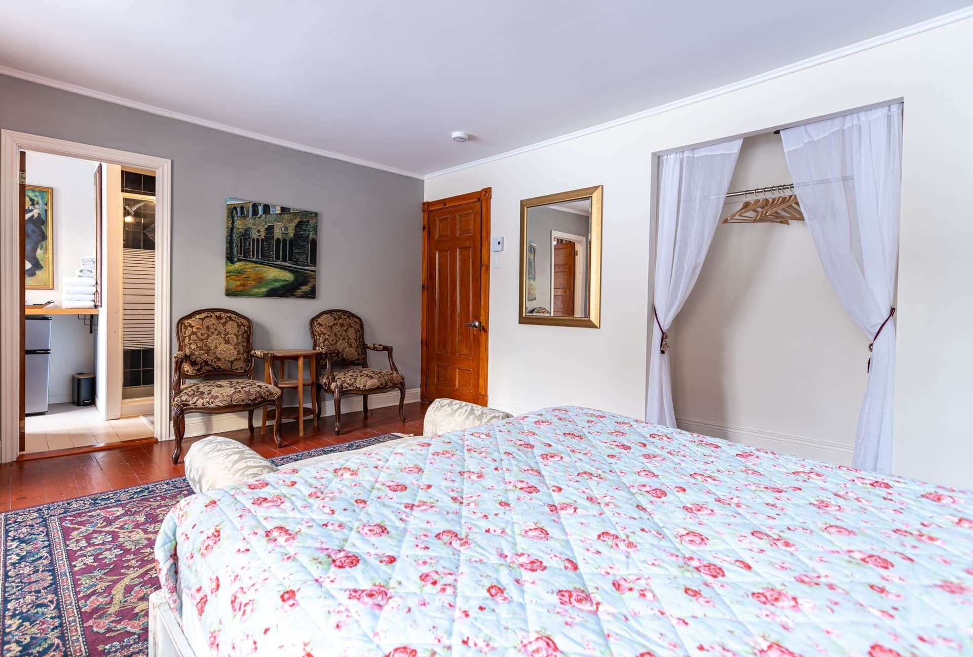Une chambre à coucher avec un lit, deux chaises, une porte en bois, un tableau et un miroir.