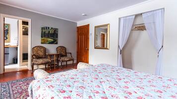Une chambre à coucher avec un lit, deux chaises, une porte en bois, un tableau et un miroir.