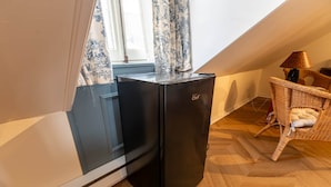 A compact kitchenette with a black refrigerator, a window with blue floral curtains, and a wicker chair with a cushion.